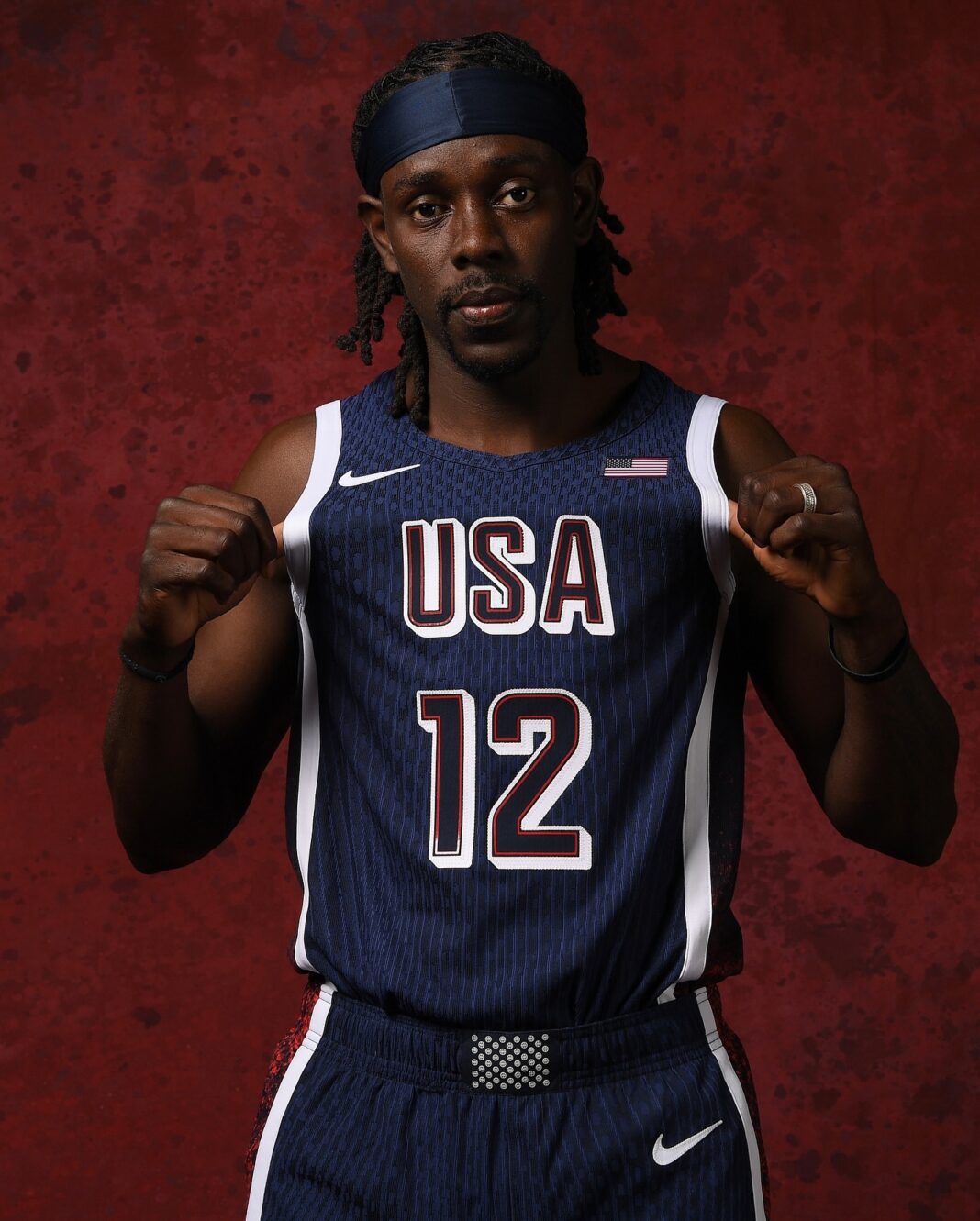 Jrue Holiday wearing a Team USA jersey during an Olympic basketball game. He is focused, dribbling the ball up the court with intensity and determination, representing the United States on the international stage. The image is part of an article by Matt Goren for All Angles, capturing Holiday's key moments in his career, including his contributions to Team USA.